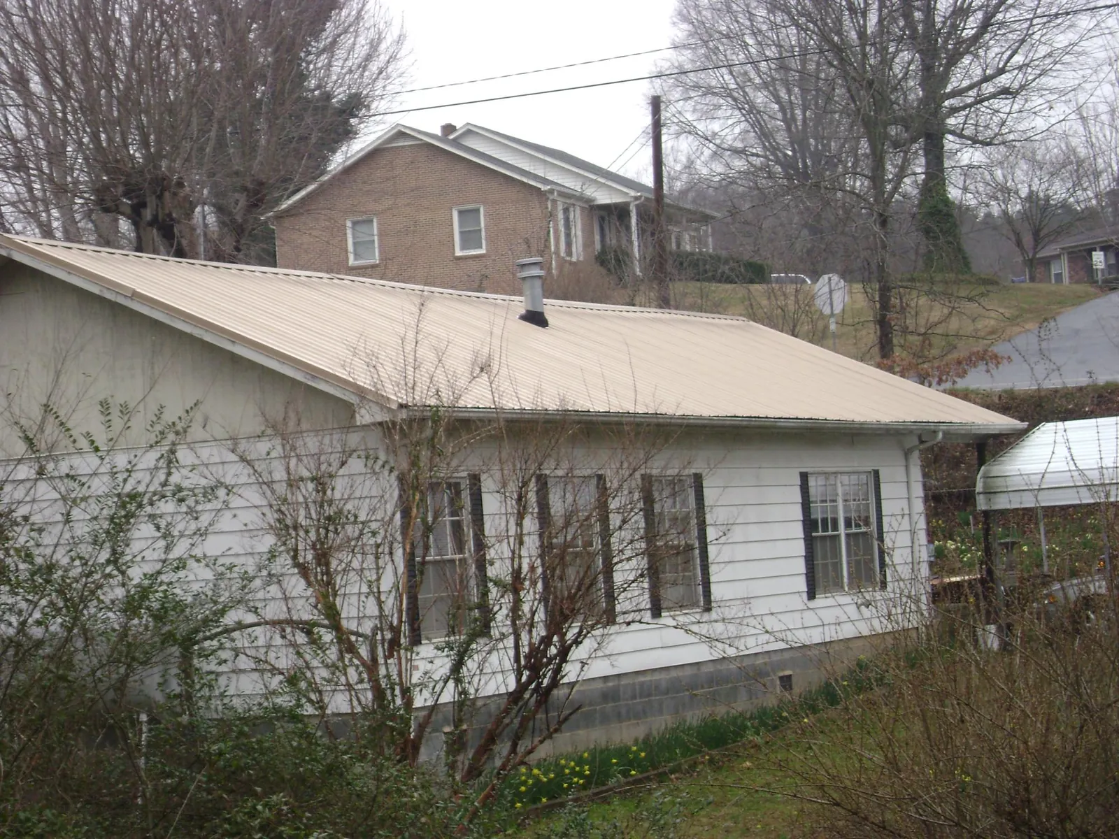 Tan metal roof on a white sided house set into a hillside — Commercial Roofing by Roofing Brothers in Cromwell